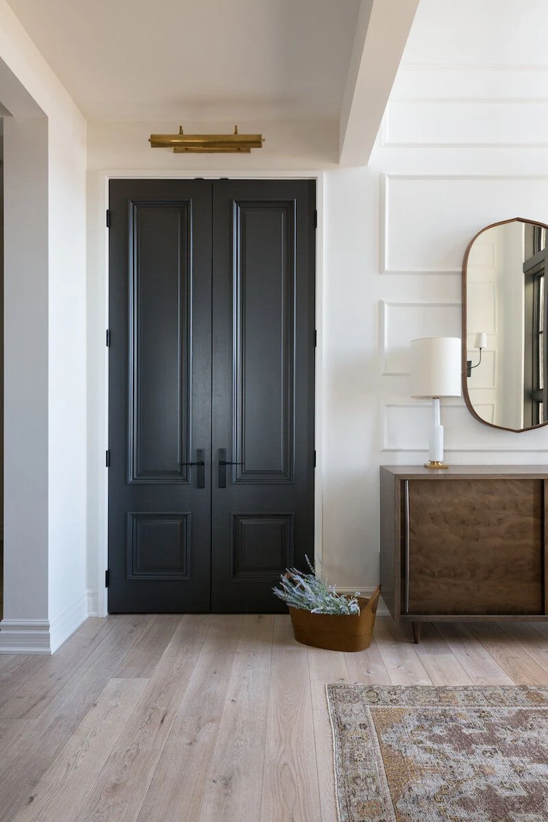 Уютен интериор с двойна врата в тъмен цвят и мебели в неутрални тонове.